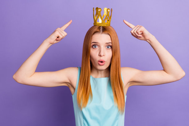 年轻迷人的女孩的照片快乐积极的微笑点手指黄金皇冠皇后皇家孤立在紫色背景图片下载