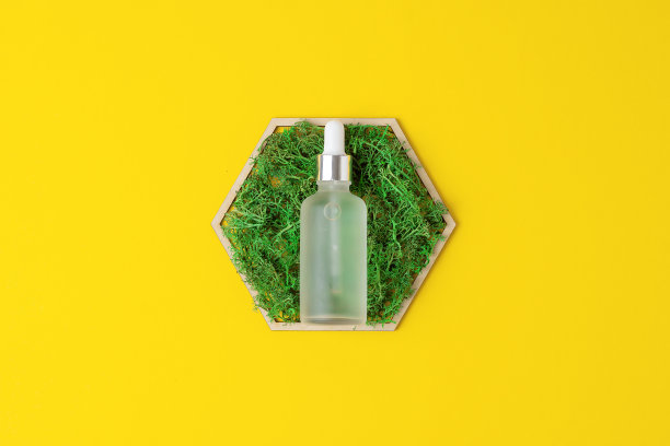 黄色背景上有木制六边形和苔藓的化妆瓶。平铺，复制空间图片下载