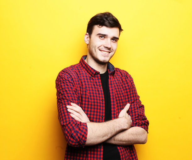 照片中的年轻男子没有刮胡子，穿着格子衬衫，双手交叉在相机前摆姿势图片下载