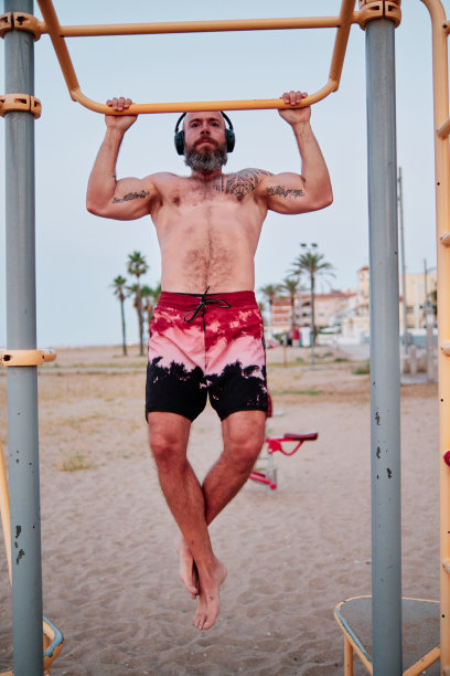 一名运动员在沙滩上做户外引体向上的同时练习健美操。图片下载