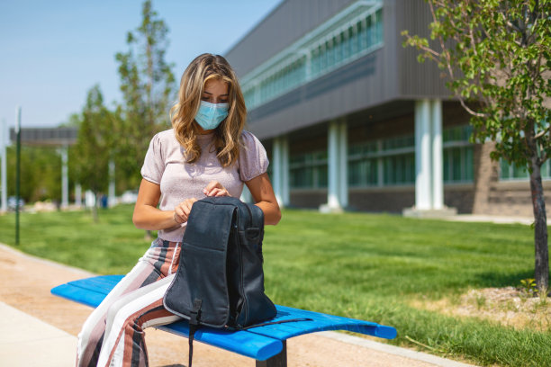 女青少年戴着口罩坐在公立学校大楼外，强制遵守重返学校照片系列图片下载