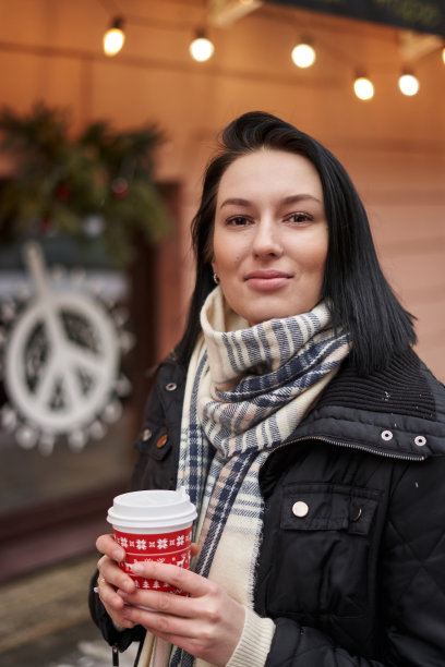 一个美丽的黑发披肩女郎在街上的特写照片，她手里拿着一个红色的纸杯图片下载