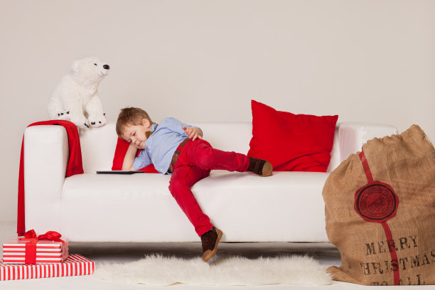 可爱的宝宝躺在沙发上，手里拿着平板电脑，期待着节日和圣诞老人。为圣诞节和新年做准备。孩子看着平板电脑的圣诞故事。节日的概念图片下载