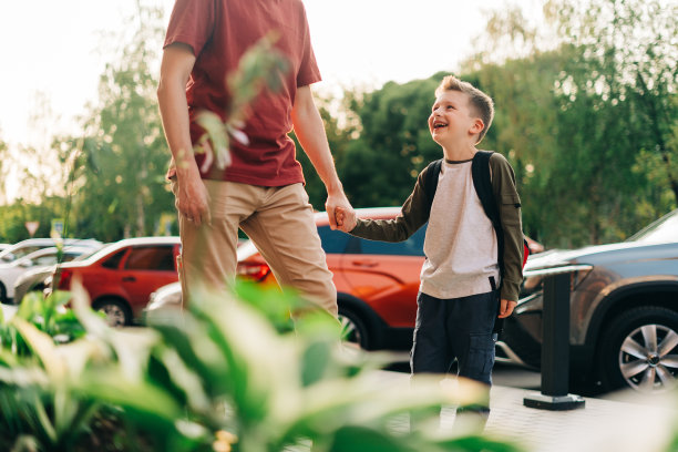 快乐的父子去上课了。一年级时，父母送孩子上学。小学生背着书包在城市街道户外学习。课的开始。回到学校图片下载