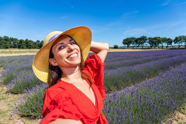 一位戴着草帽的美女在盛开的薰衣草地里自拍。图片下载