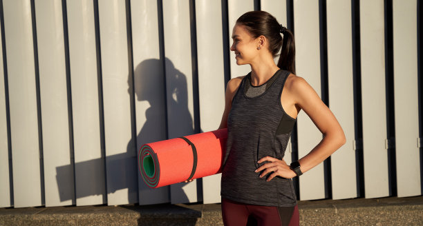 快乐美丽的女人抱着运动垫在户外图片下载