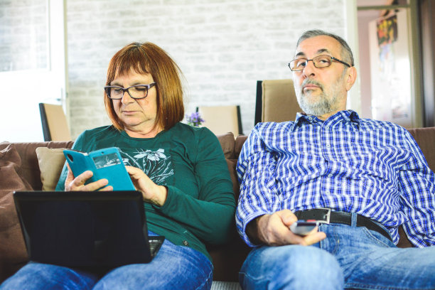 老夫妇一起坐在家里客厅的沙发上用笔记本电脑放松。图片下载