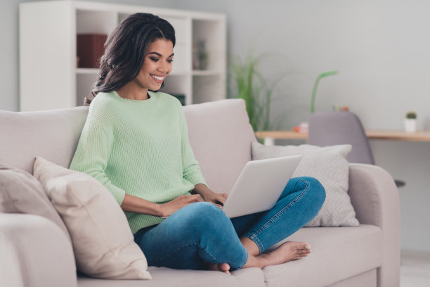 全尺寸照片迷人开朗的深色皮肤女士使用笔记本电脑阅读有良好的心情工作，从家里室内图片下载