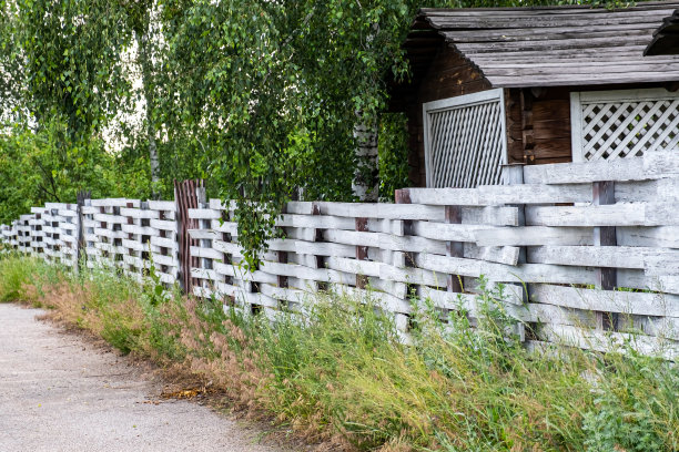 白色的柳条篱笆在房子附近的绿色背景下。图片下载
