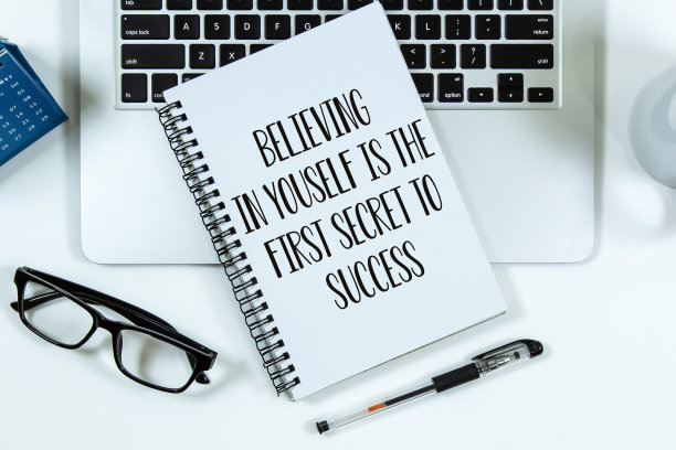 “相信自己是成功的第一秘诀”在笔记本上的文字和办公室桌上的笔记本电脑。图片下载