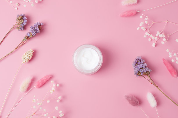 粉红色背景上有花的化妆霜。平铺，复制空间图片下载