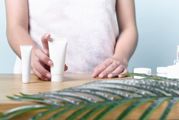 年轻女子一手拿着包装在桌上的奶油产品。护肤产品中的安全概念。图片下载