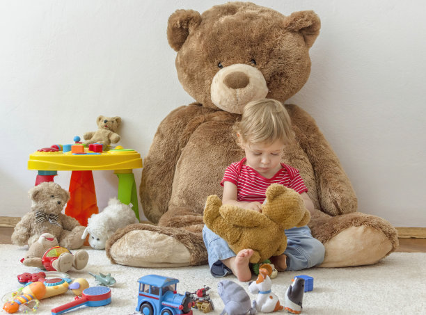 甜美快乐的小男孩在家里玩他的巨型泰迪熊和许多五颜六色的玩具图片下载
