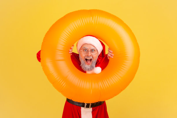 灰胡子老人的肖像穿着圣诞老人的服装，表现出惊诧震惊的表情，在温暖的度假胜地庆祝冬季假期。图片下载
