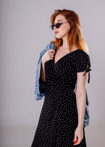 一个身穿黑色连衣裙的黑发女孩站在白色背景下，手里拿着一件牛仔夹克。图片下载