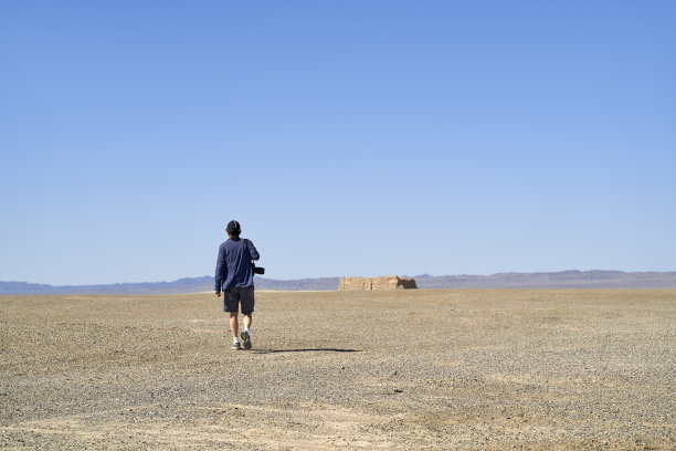 亚洲男性摄影师在戈壁沙漠行走的后视图图片下载
