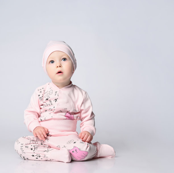 一个穿着长袖和shianishka的婴儿坐在工作室的地板上，他戴着一顶配套的帽子，衣服上有一个有趣的孩子气的图案图片下载