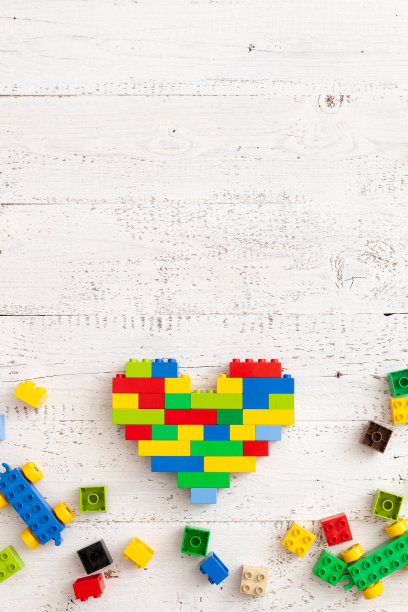 彩色的塑料方块散落在一张白色的木桌上。一个聪明的建筑家设计的心形创意建筑。早期的学习。益智玩具图片下载