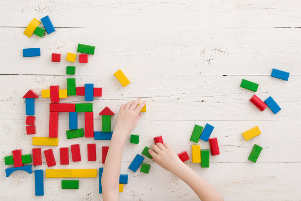 俯视图在一个孩子的手建立一个城堡，五颜六色的木块分散在一个白色的木桌。学校、教育和培训理念。自我隔离和流行病期间的家庭游戏图片下载