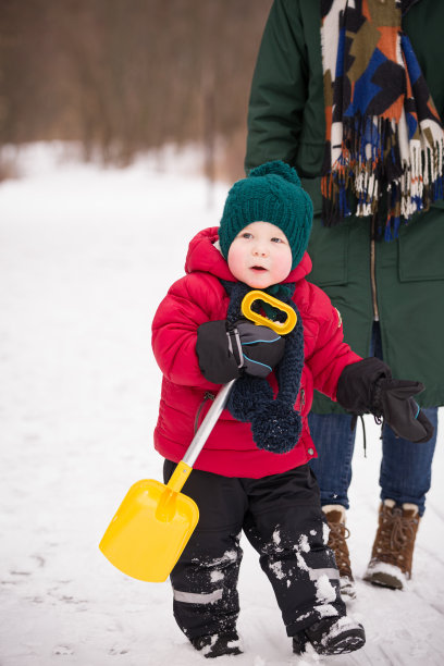 一个可爱的小女孩和妈妈在公园里散步。穿着红色夹克，手里拿着铲子的小孩。冬季儿童户外活动图片下载