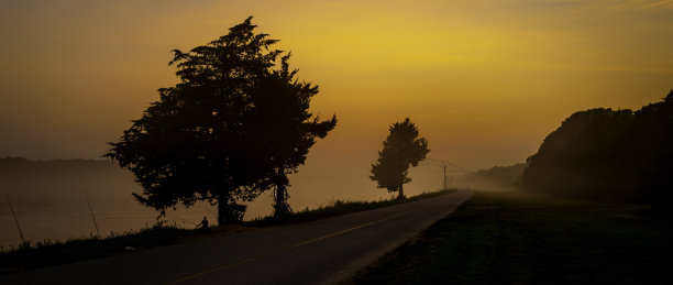 全景日出海景在雾蒙蒙的科德角运河。树木、小山和河岸的剪影。雾蒙蒙的灰色运河和橘色的天空。图片下载