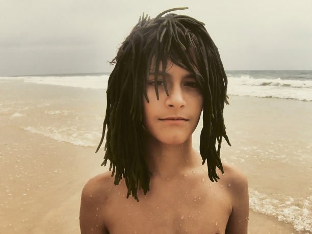 沙滩上的男孩戴着海草做的假发图片下载