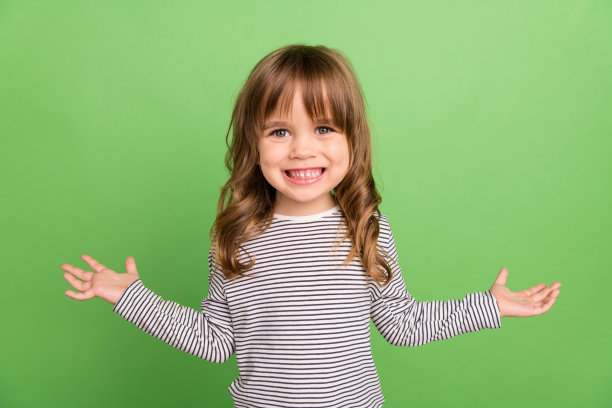 照片中有趣的金发小女孩双手拥抱穿着条纹衬衫孤立在绿色背景上图片下载