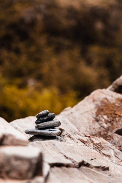 在一个模糊的秋天森林背景的岩石表面上平衡的岩石(岩石cairn)的垂直照片图片下载