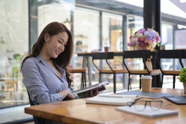 微笑的年轻亚洲女人在现代咖啡店看书。图片下载