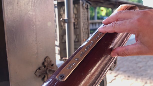 视障白人盲人男性阅读火车站台楼梯扶手上的金属触觉辅助板上的盲文字母指示标志图片下载