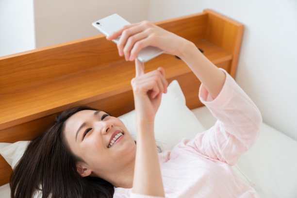 漂亮的亚洲女人在床上用智能手机图片下载