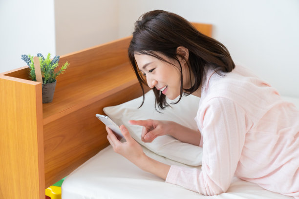 漂亮的亚洲女人在床上用智能手机图片下载