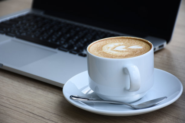 带笔记本电脑的桌面工作区。木桌上放着杯白咖啡。图片下载