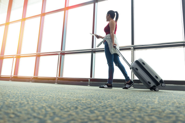 一个年轻的女人站在机场的窗边，注视着即将起飞的飞机。她拿着行李站着。旅游的概念图片下载