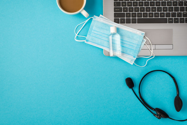 顶视图照片的消毒剂瓶，医用口罩膝上型耳机和一杯咖啡孤立的淡蓝色背景与copyspace图片下载