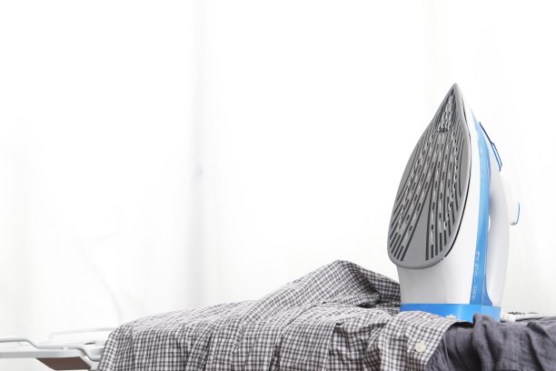 电熨斗和一堆衣服在熨衣板和白色背景图片下载