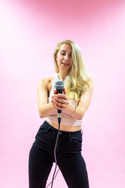 漂亮的年轻女子拿着麦克风在粉红色的背景下唱歌图片下载