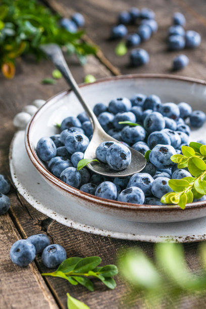 碗里新鲜采摘的蓝莓。多汁的新鲜浆果和绿叶放在质朴的餐桌上。健康食品和营养观念图片下载