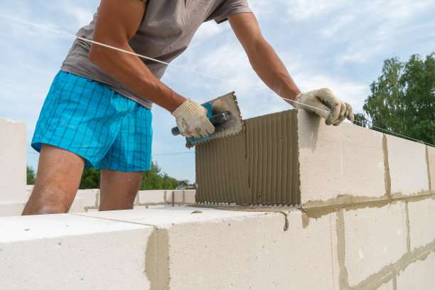 施工人员用带槽的镘刀将水泥混合物涂抹在砌块的一侧。建造房屋的概念图片下载