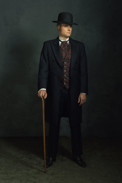 穿着时髦复古维多利亚服装的年轻人。拄着拐杖站在一间屋子里，前面是一堵深灰色的墙。图片下载