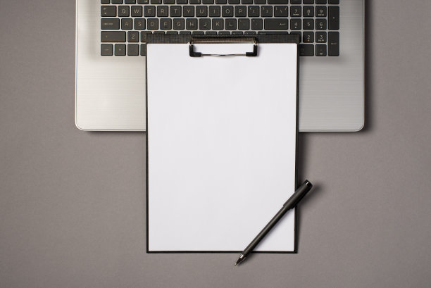 顶视图照片的黑色剪贴板文件夹与白色的纸页和笔在灰色的笔记本电脑键盘上孤立的灰色背景与空白图片下载