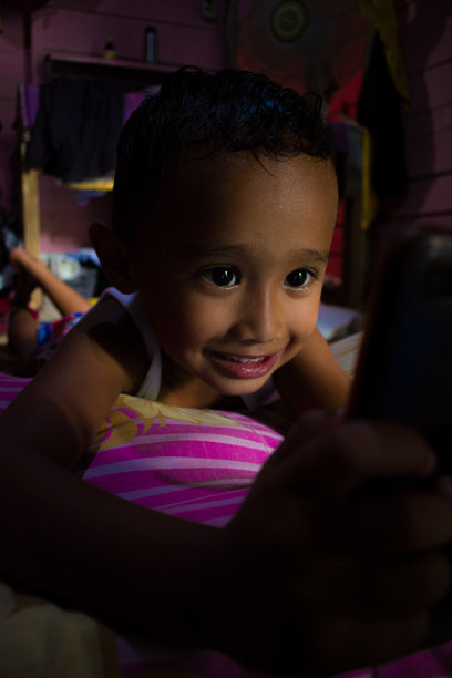 小男孩微笑着躺在床上玩手机图片下载