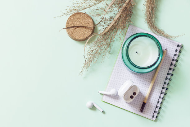 在柔和的绿色背景上，平躺着静物芳香蜡烛、蒲苇、记事本和铅笔。模型，照片与中性调色板。副本的空间。图片下载