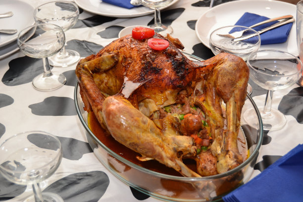 装有感恩节烤火鸡的玻璃托盘上装饰着西红柿，放在装饰节日的桌子上图片下载
