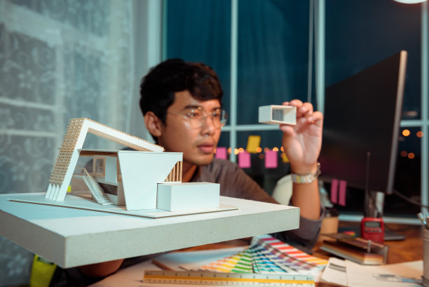 建筑师-设计师在晚上工作，用现代箱子屋的模型，同时思考未来开工前的建筑概念和施工项目。图片下载