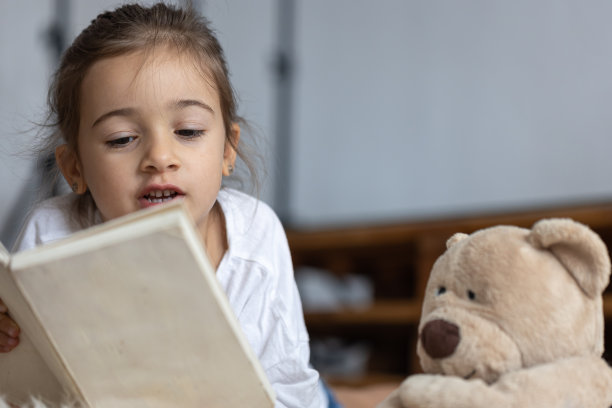 小女孩和泰迪熊一起看书。图片下载