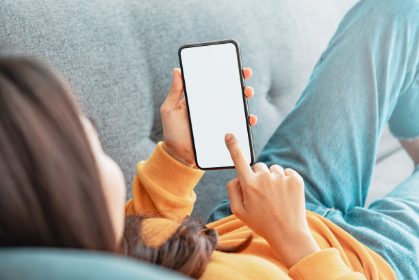 一名妇女在客厅的沙发上使用带有空白屏幕的手机。图片下载