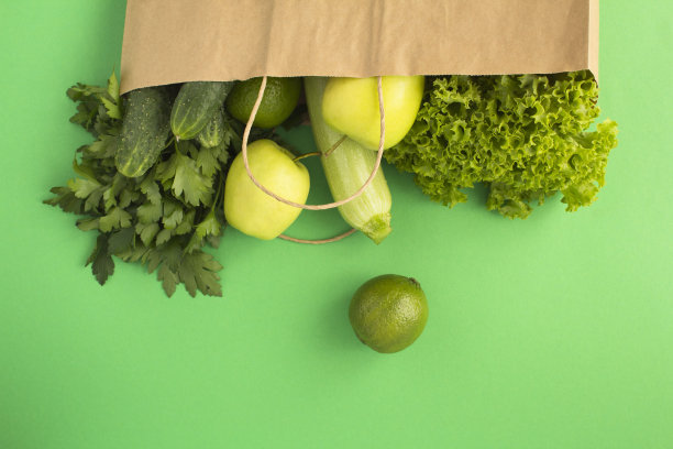 绿色背景上有绿色蔬菜和水果的纸袋。前视图。图片下载