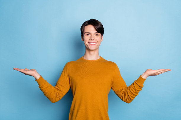 开朗的家伙的照片两手掌举着看不见的物体空的空间穿着橙色衬衫孤立的蓝色背景图片下载