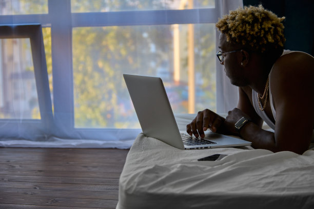 一个黑人在床上用笔记本电脑工作图片下载